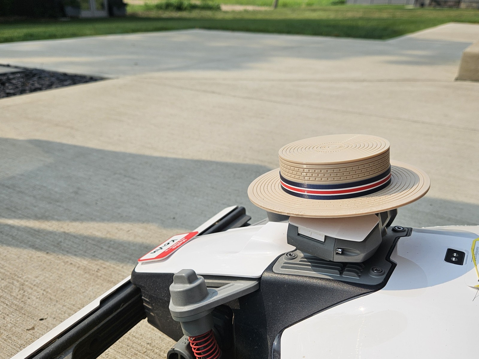 Kevin, a Mammotion Luba robot mower, wearing a 3D-printed straw boater hat on a cut lawn